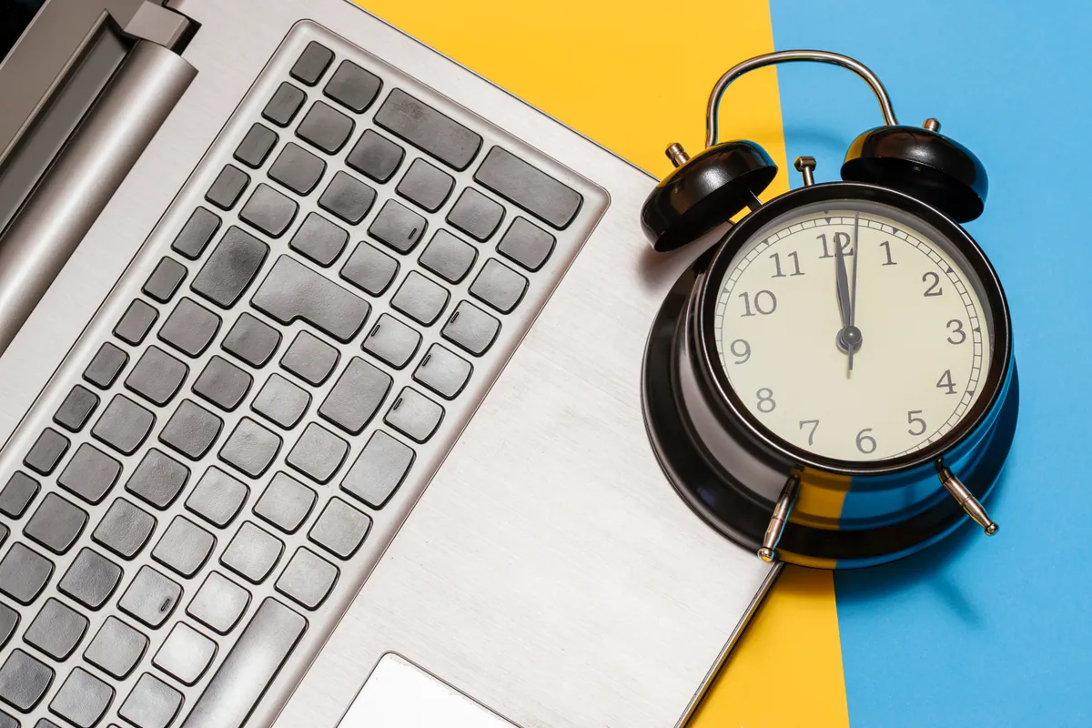 An alarm clock beside a laptop, illustrating the timing of computer repairs