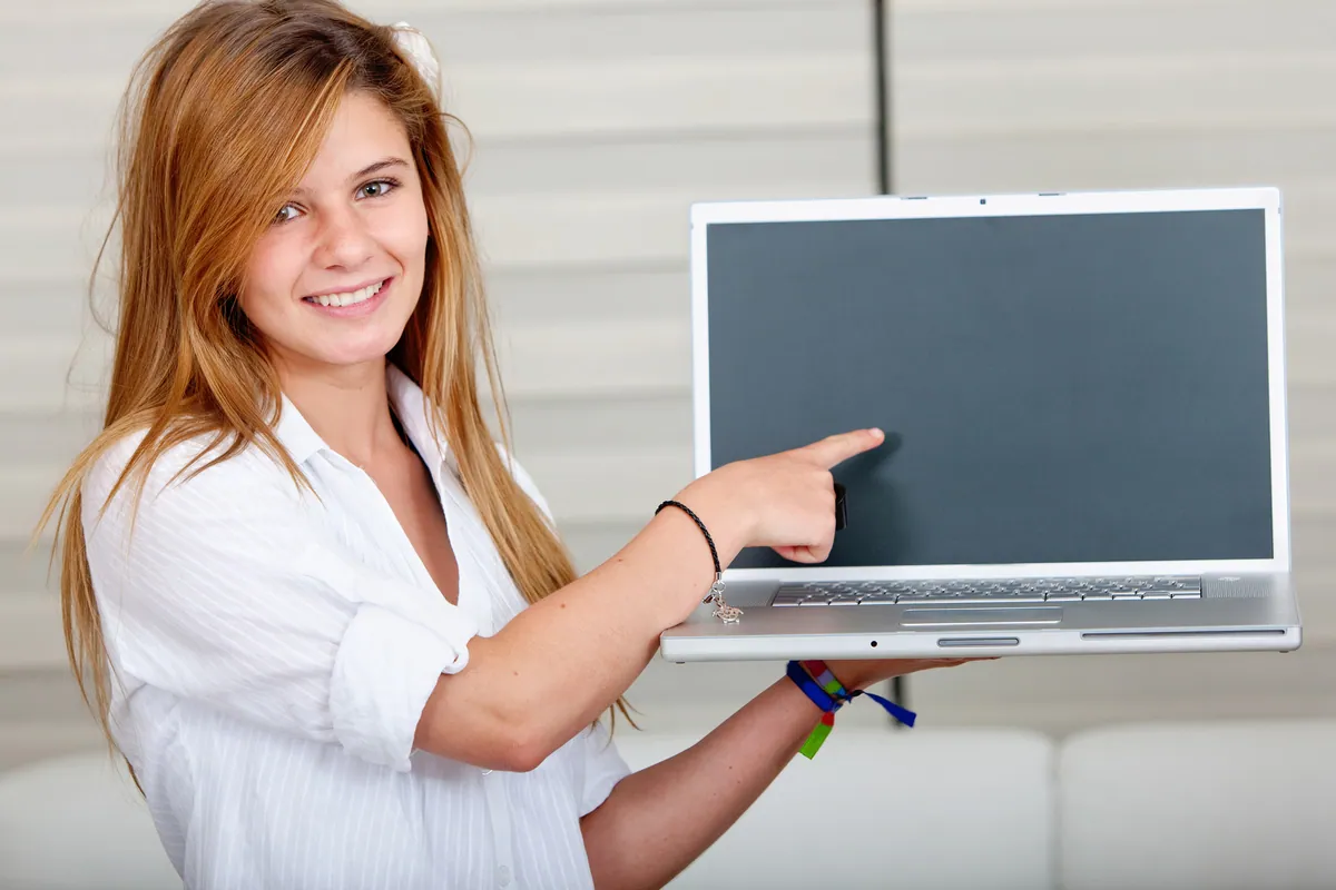 A smiling young student holding a laptop, ready for the new school term