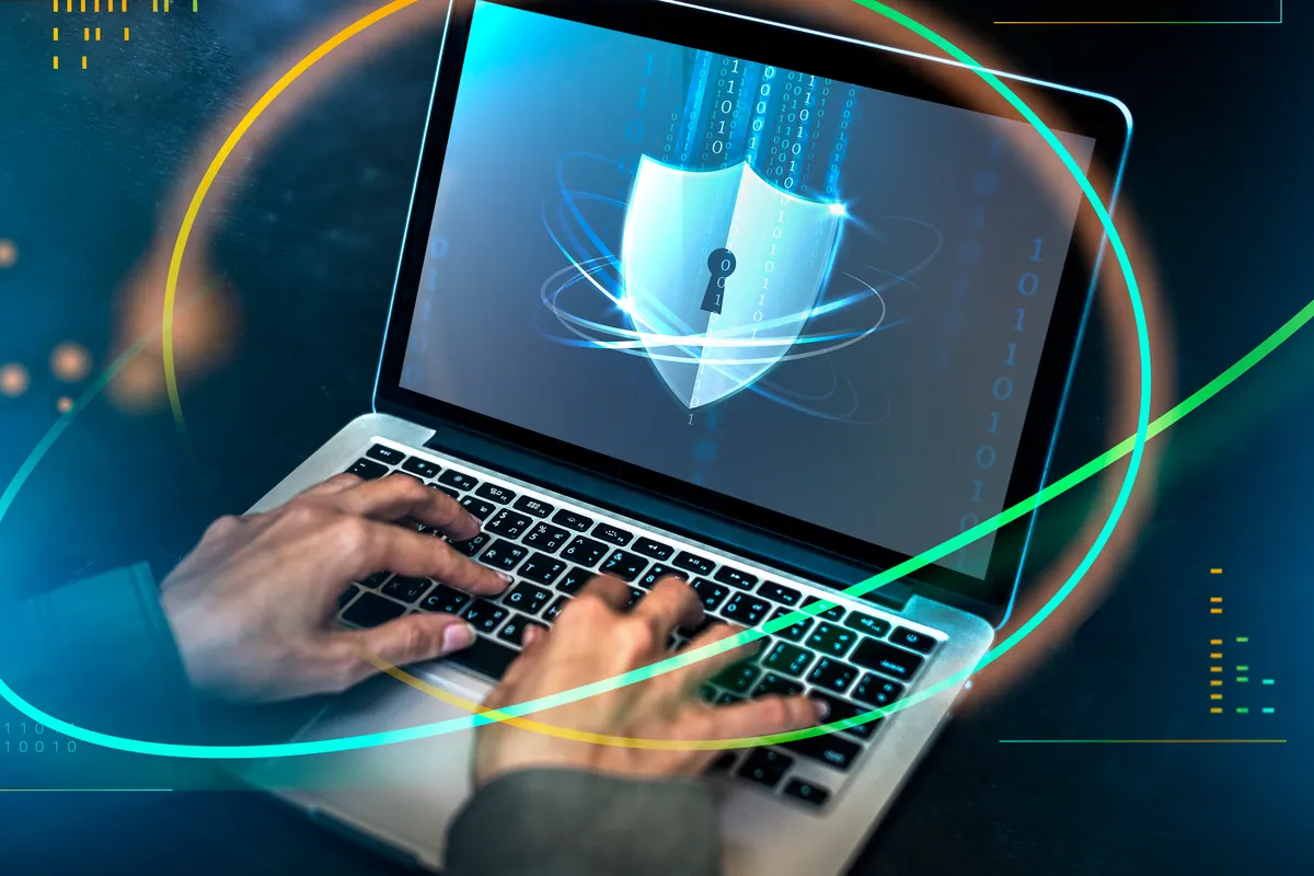 Hands typing on a laptop with a security shield icon