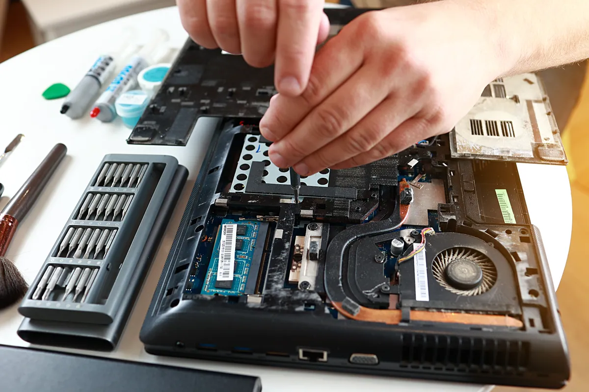 A laptop opened up on a workbench with precision screwdrivers for repair