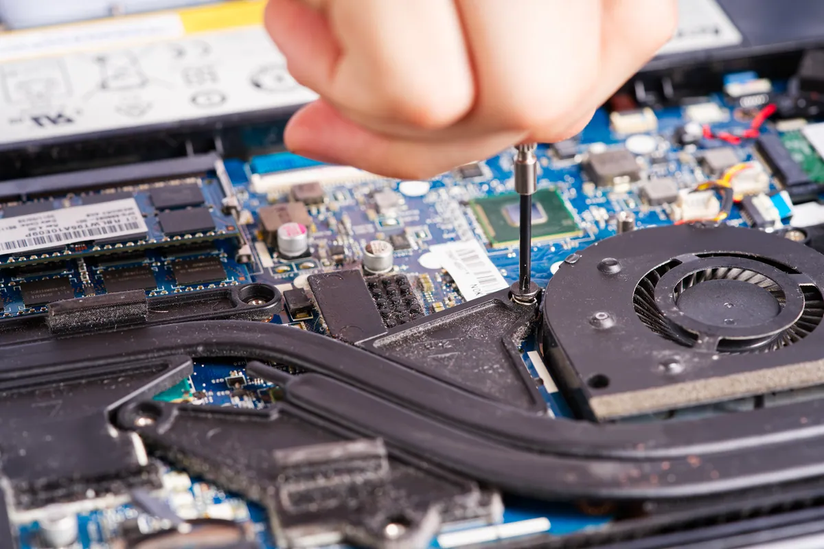 A technician's hands repairing a laptop motherboard