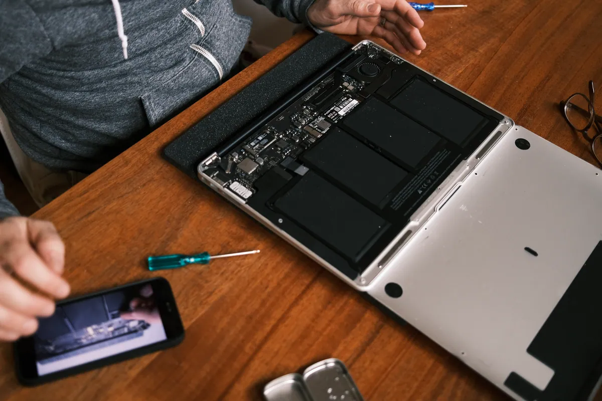 A technician replacing internal parts on a dismantled laptop