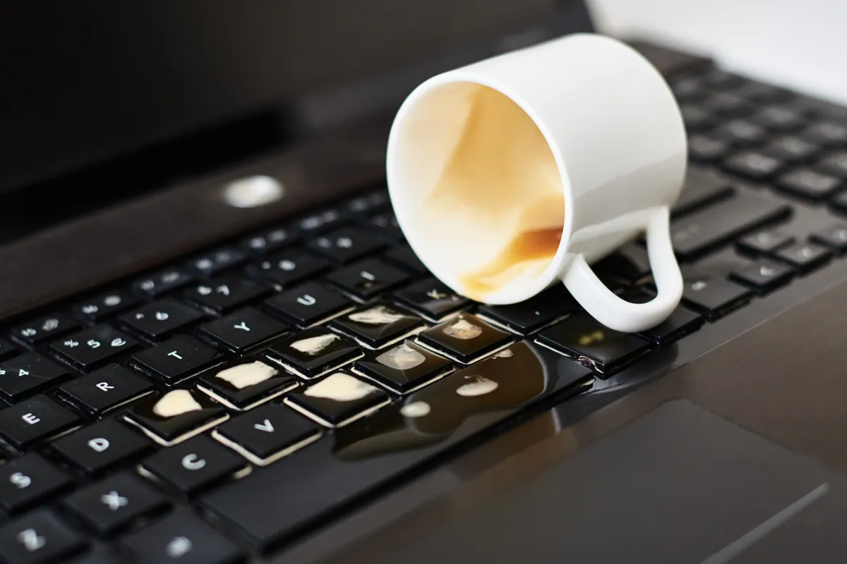 Coffee spilling from a white cup onto a laptop keyboard