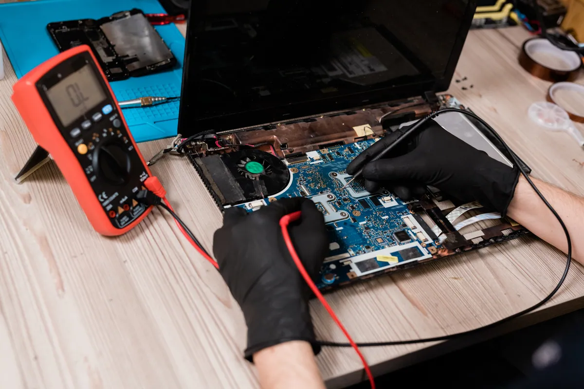 Laptop motherboard being tested with a multimeter on a workbench